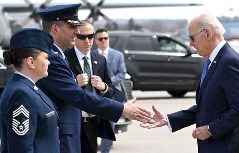 President Joe Biden presents his challenge coin to a service member in a "coin handshake" upon his arrival on an airfield tarmac.